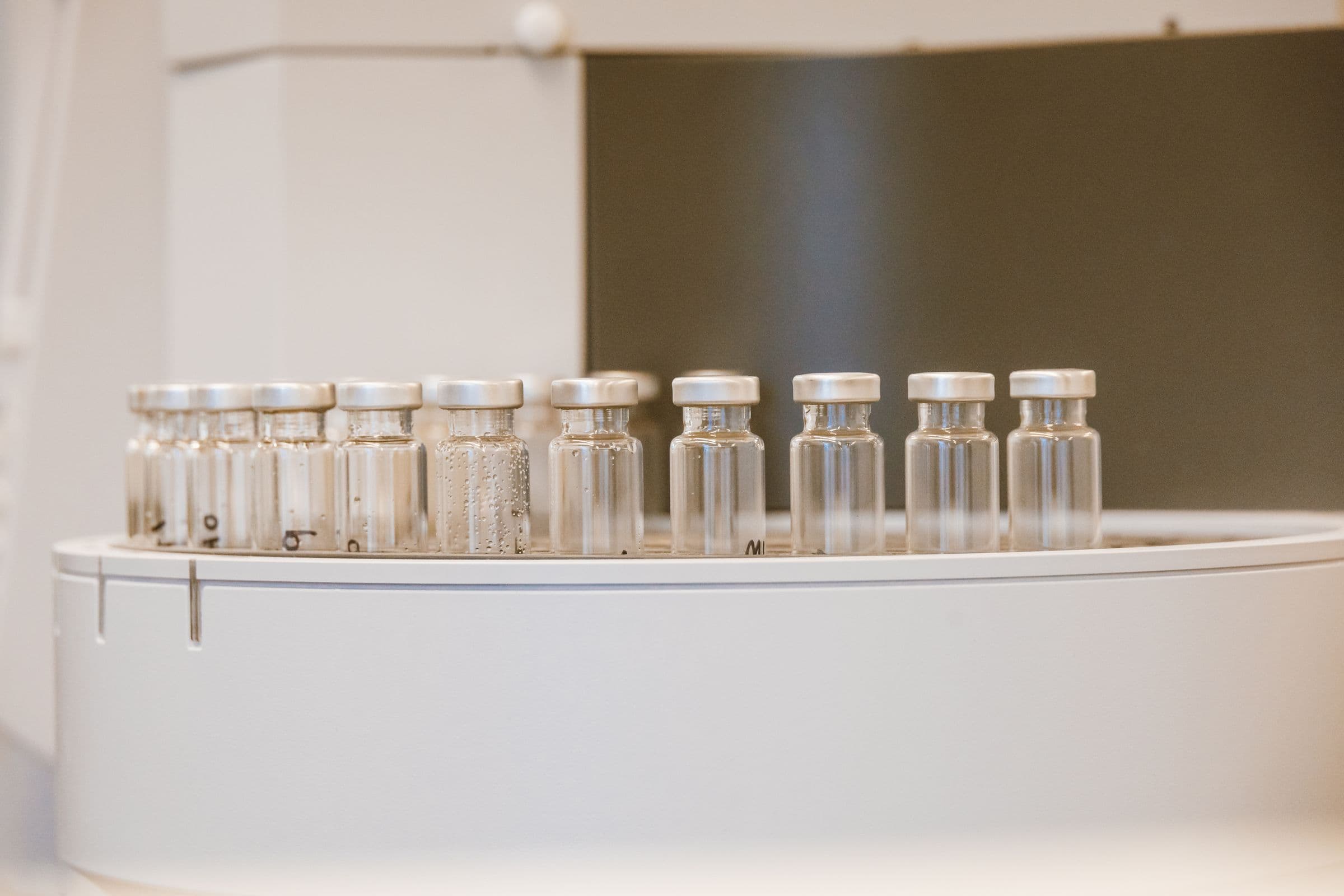 Row of crimp-capped clear glass vials on a laboratory instrument tray