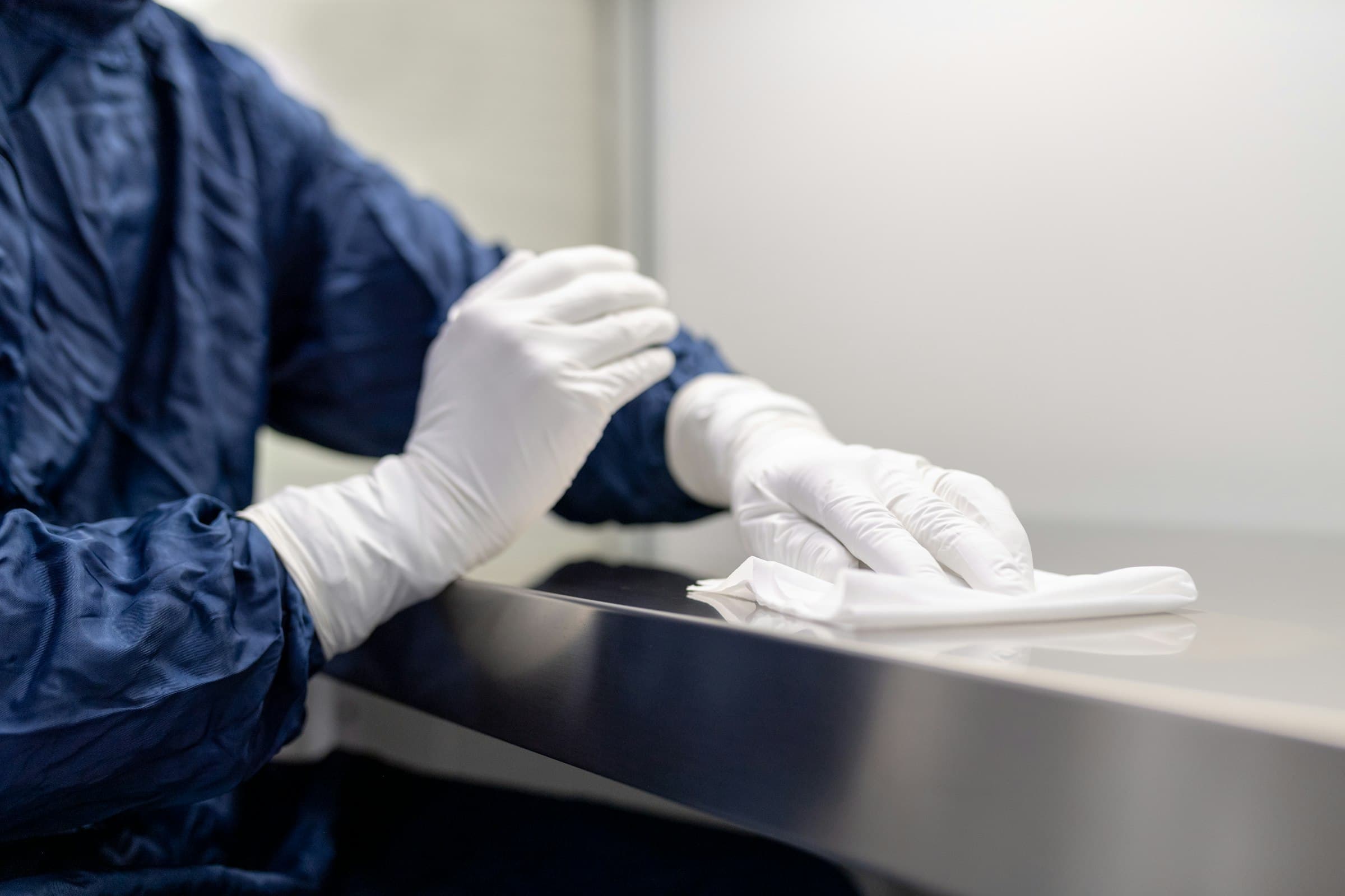 Gloved hands wiping down a stainless steel cleanroom surface